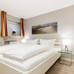 Schlafzimmer mit weißem Bett, Fenster und Wandbild.