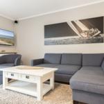 Wohnzimmer mit grauem Sofa, weißem Couchtisch und Wandbild mit Segelboot.