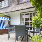 Terrasse mit Gartenmöbeln und Strandkorb vor einem Haus mit Strohdach.