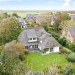 Haus mit Strohdach und Garten. Blick auf Felder und Meer.