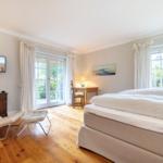 Schlafzimmer mit Bett, TV und Schreibtisch. Holzboden und große Fenster.