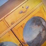 Holzschrank mit zwei Schubladen und runden Fenstern mit Malereien.