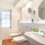 Badezimmer mit Waschbecken, Toilette, Bidet und Dusche. Fenster mit Jalousie. Holzboden.