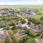 Dorf mit strohgedeckten Häusern und grünen Wiesen im Hintergrund.