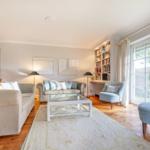 Wohnzimmer mit Sofa, Sessel und Bücherregal. Holzboden und große Fenster.