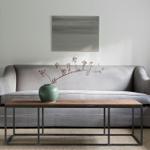 A gray sofa with a wood and metal table in front. A painting hangs behind the sofa.