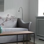 Gray sofa with wooden table and vases. Window and radiator are visible.