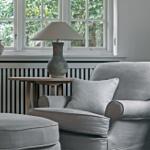 A gray armchair with cushion and ottoman in front of a window with a view of trees.
