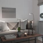 Living room with sofa, table, candles, and flowers. Window with view of greenery.
