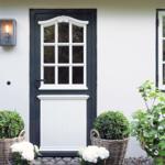 Front door with white windows and potted plants against white wall.