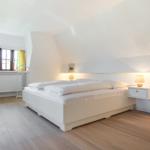 Schlafzimmer mit Doppelbett, Nachttischen und Fenster mit gelben Vorhängen.