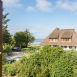 Durch das Fenster ist das Haus mit Strohdach und Blick aufs Meer zu sehen.