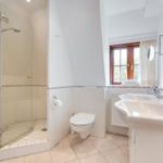 Badezimmer mit Dusche, Toilette und Waschbecken. Fenster mit Holzrahmen.