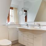 Badezimmer mit Waschbecken, Spiegel, Toilette und Fenster.