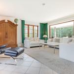 Wohnzimmer mit weißen Sofas, grünen Vorhängen und Holzschrank.