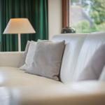 Weißer Ledersofa mit Kissen vor Fenster mit grünen Vorhängen.