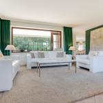 Wohnzimmer mit weißen Sofas, grünen Vorhängen und großer Wanddekoration.