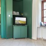 Ein Raum mit grünem Schrank, Fernseher und Fenster mit weißen Vorhängen.