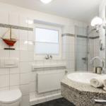 Badezimmer mit Dusche, Waschbecken und Toilette. Wanddekoration mit Segelboot.