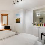 Schlafzimmer mit Bett, Schrank und Stuhl. Wandbild und Spiegel sichtbar.