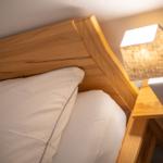 Hölzernes Bett mit weißer Bettwäsche und Nachttisch mit Lampe.