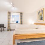 Schlafzimmer mit Holzbett, Fenster mit Vorhängen und Wandbild.