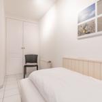 Schlafzimmer mit weißem Bett, Kleiderschrank und Wandbildern.