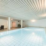 Innere Schwimmhalle mit Pool, Sitzgelegenheiten und Wandmalerei.