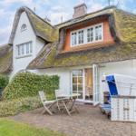 Haus mit strohgedecktem Dach, Terrasse mit Tisch, Stühlen und Strandkorb.