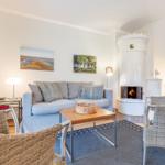 Wohnzimmer mit Sofa, Kamin und Stühlen. Wandbilder und Teppich sind sichtbar.