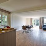 Kitchen with dining area and living room with wooden floor and windows.