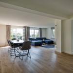 Large living and dining area with wooden floor and blue sofa.