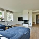 Living room with blue sofa, fireplace, and wooden floor. Kitchen in the background.