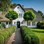 White cottage with thatched roof, manicured garden, and gravel path to the entrance door.