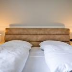 Two beds with white bedding and brown headboard. Both sides have nightstands with lamps.