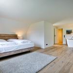 Bedroom with bed, rug, and bathroom. Wooden floor and white walls.