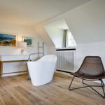 Attic room with freestanding bathtub, chair, and window.