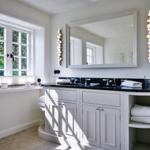 Bathroom with white vanity, mirror, and window overlooking trees.