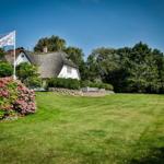 A white house with thatched roof, surrounded by grass and flowers.