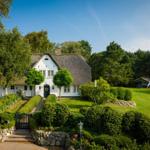 White house with thatched roof, manicured garden, and trees in the background.