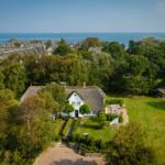 House with thatched roof, surrounded by greenery and trees, view of the sea.