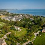 Aerial view of holiday homes by the sea with green gardens and trees.