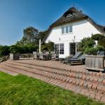 House with thatched roof and terrace with loungers and table.
