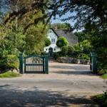 A white house with a thatched roof behind a green gate and stone walls.