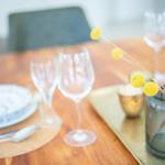 Holztisch mit Geschirr, Gläsern und gelben Blumen in einem Glas.