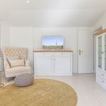 Ein Wohnzimmer mit Sessel, Fernseher und Schrank. Fenster und Teppich sind sichtbar.
