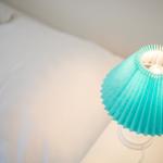 Eine blaue Lampe neben einem Bett mit weißer Bettwäsche.
