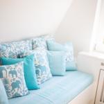 Sitzbank mit blauen Kissen und Elefantenmuster unter Fenster