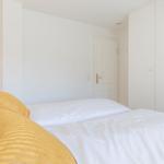 Schlafzimmer mit weißem Bett, gelben Kissen und Schrank