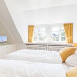 Zimmer mit Dachschrägen, Fenster und Bett mit gelben Kissen.